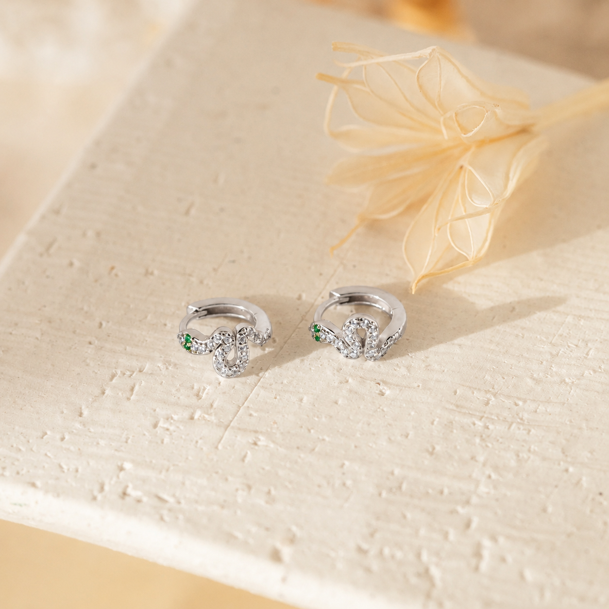 Silver earrings with green gemstones on a textured beige surface